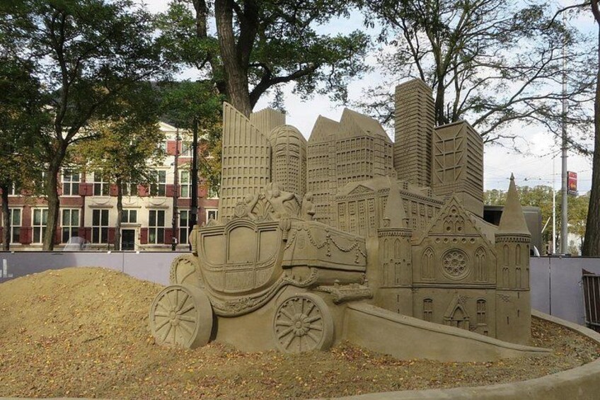 En sandskulptur som föreställer en stadsbild med byggnader och en hästdragen vagn. 5