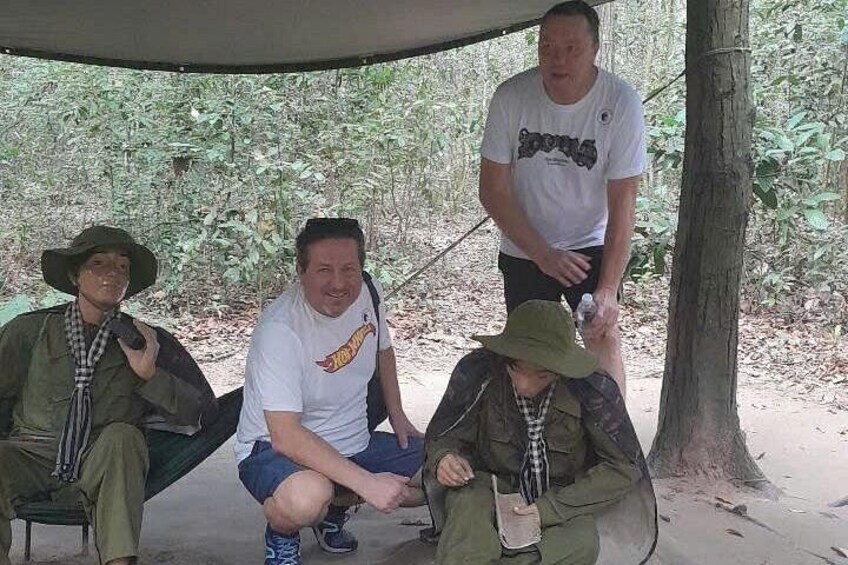 Cuatro personas sentadas bajo una carpa en un área boscosa. 3