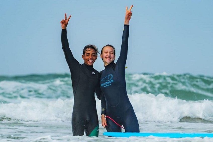 Two people in wetsuits on a surfboard with waves in the background. 4