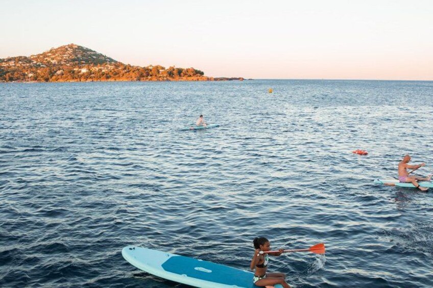 Escena costera con gente en el agua, una tabla de surf y una colina distante. 2