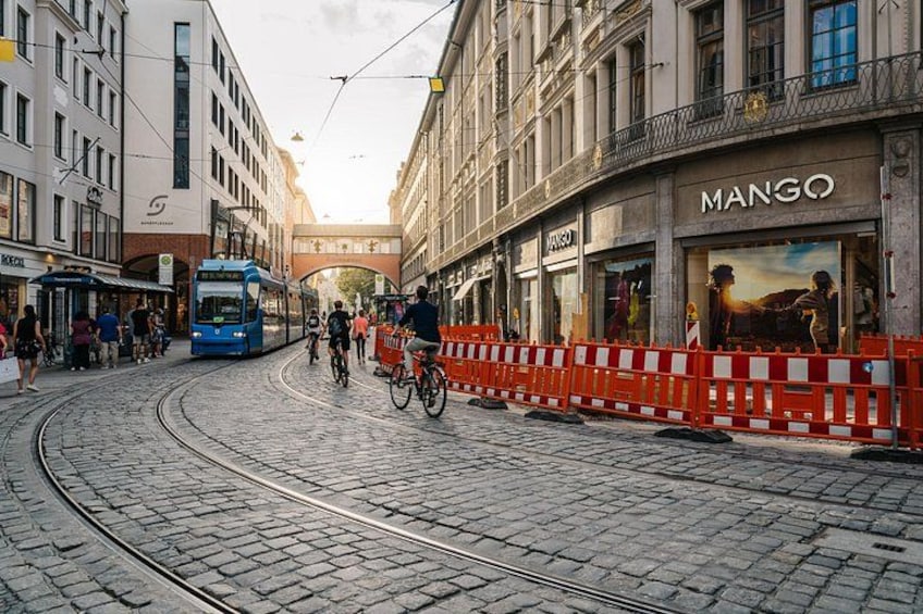Una calle adoquinada con un tranvía, una tienda de mangos y una persona montando en bicicleta. 3