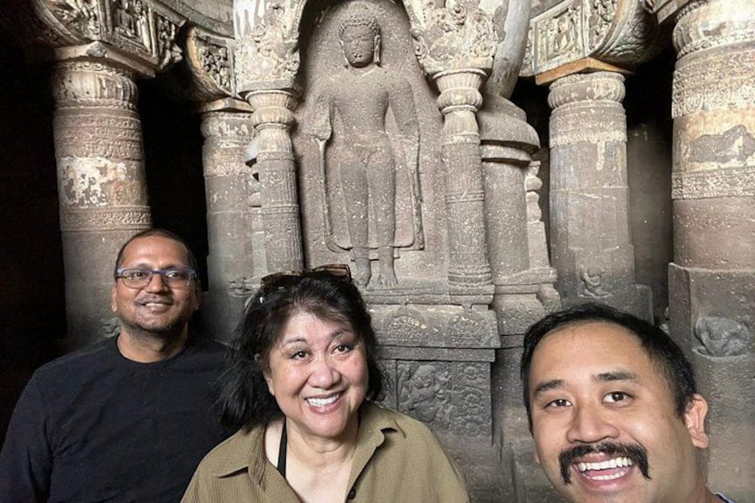 Three people standing in front of a stone structure with intricate carvings and a large statue. 3