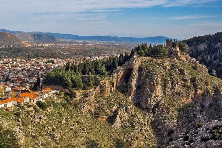 A mountainous landscape with a town at the base, a prominent rocky hill with ruins, and distant mountains. 5