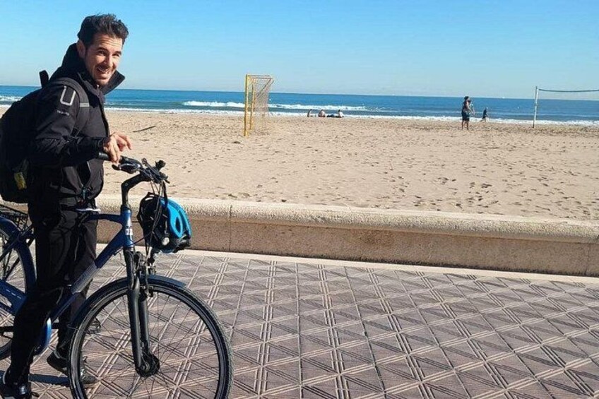 Eine Person mit Fahrradhelm am Strand, mit einem Volleyballnetz und dem Meer im Hintergrund. 1