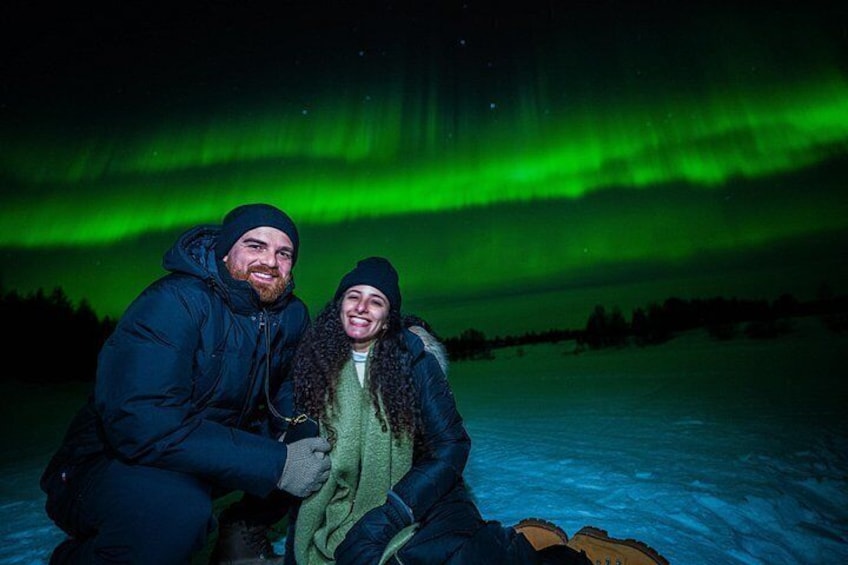 Two people sitting on snow with the aurora borealis in the background. 3