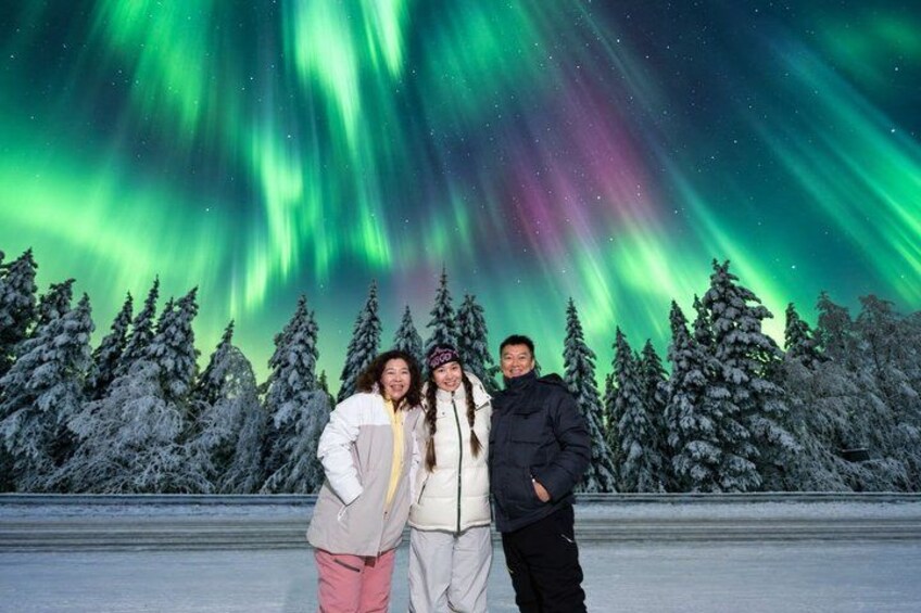 Three people standing in a snowy landscape with a view of the northern lights. 2