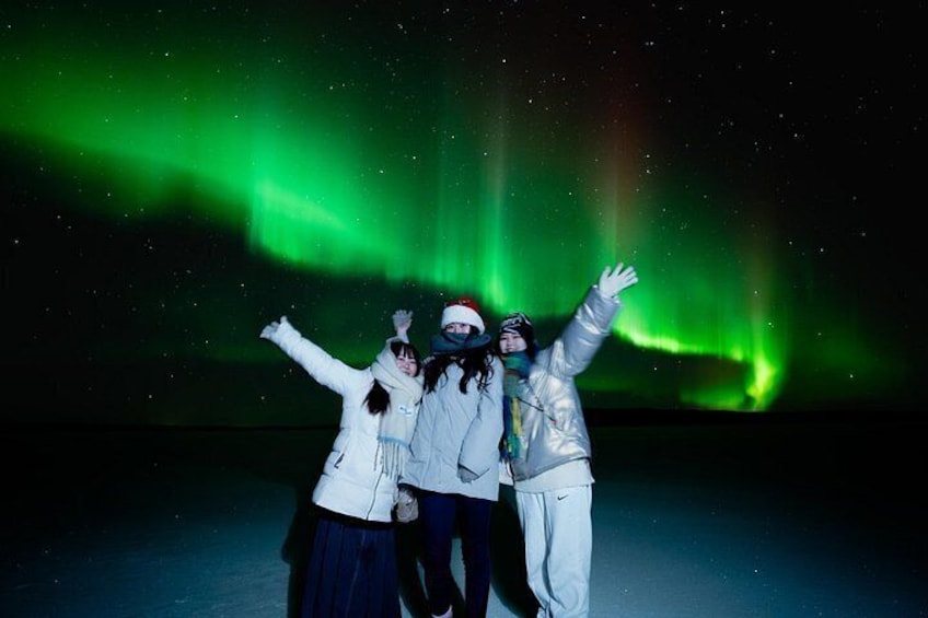 Three people posing with arms raised against a night sky with green aurora borealis. 2