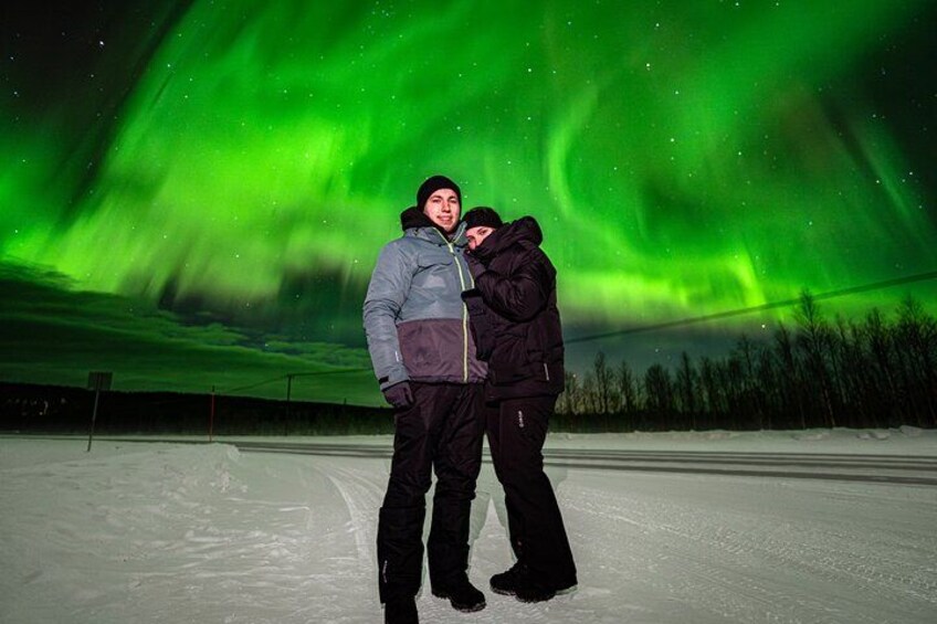 Two people standing on a snowy surface with a green aurora in the background. 5
