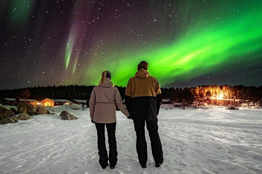 Two people walking on snow with the Northern Lights in the background. 5