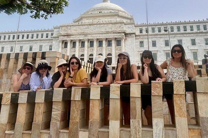 A group of people leaning on a stone fence in front of a large white building with columns and a dome. 3