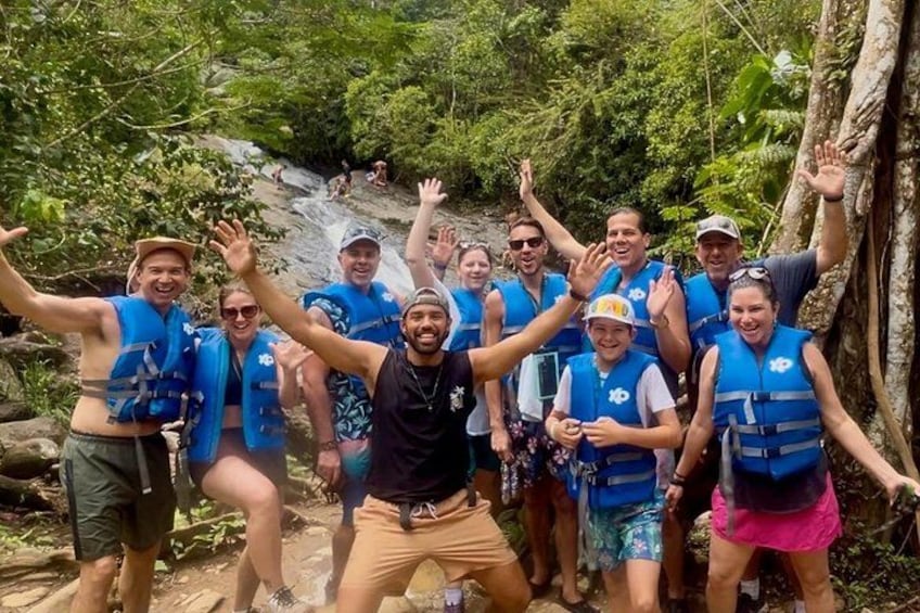 Un gruppo di persone con giubbotti di salvataggio blu che posa in una zona boschiva con una cascata sullo sfondo. 2