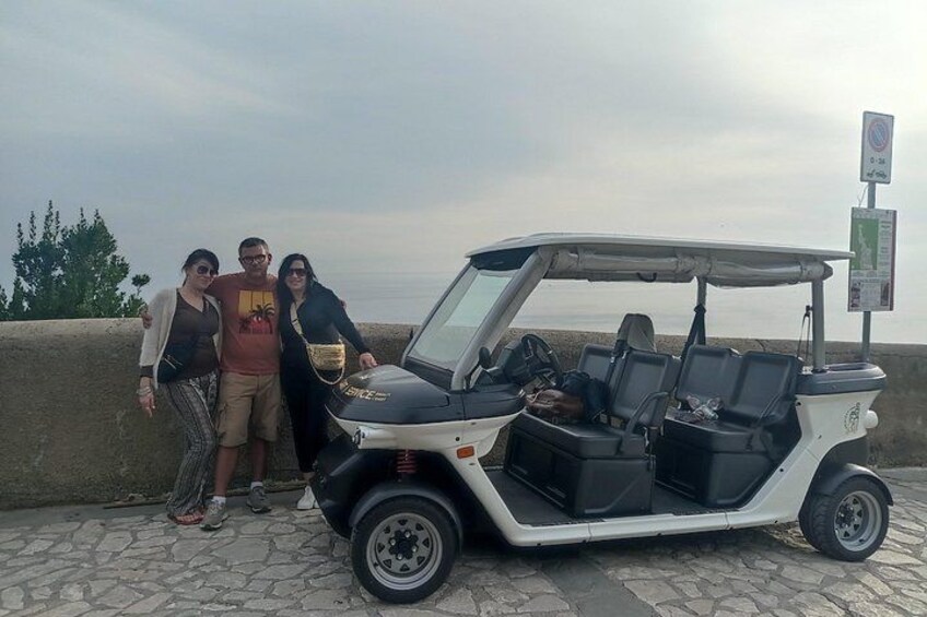 A golf cart parked on a paved area with a group of people standing beside it. 5