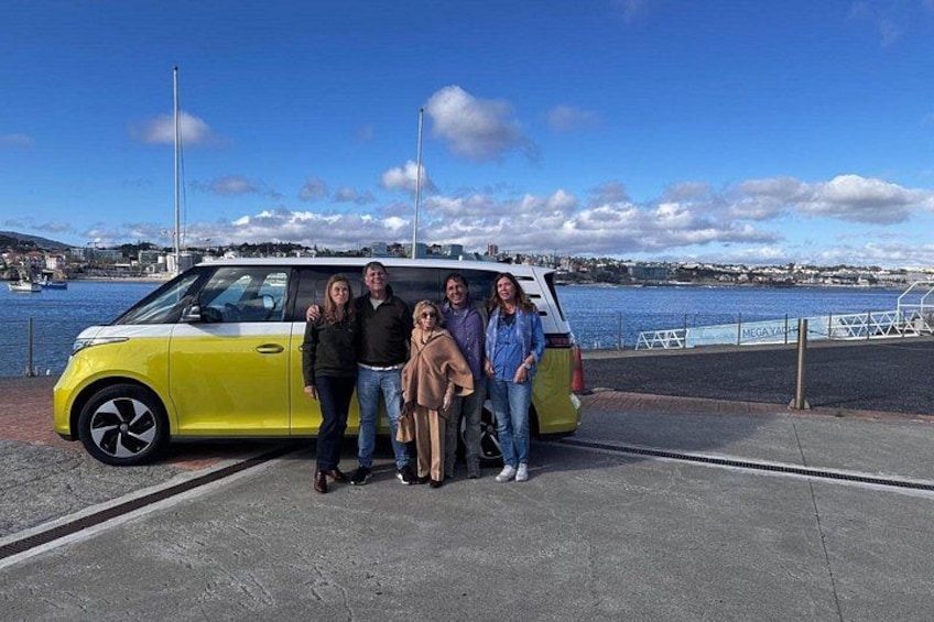 Un véhicule jaune est garé au bord de l’eau, sous un ciel dégagé, avec des bâtiments visibles au loin. 1