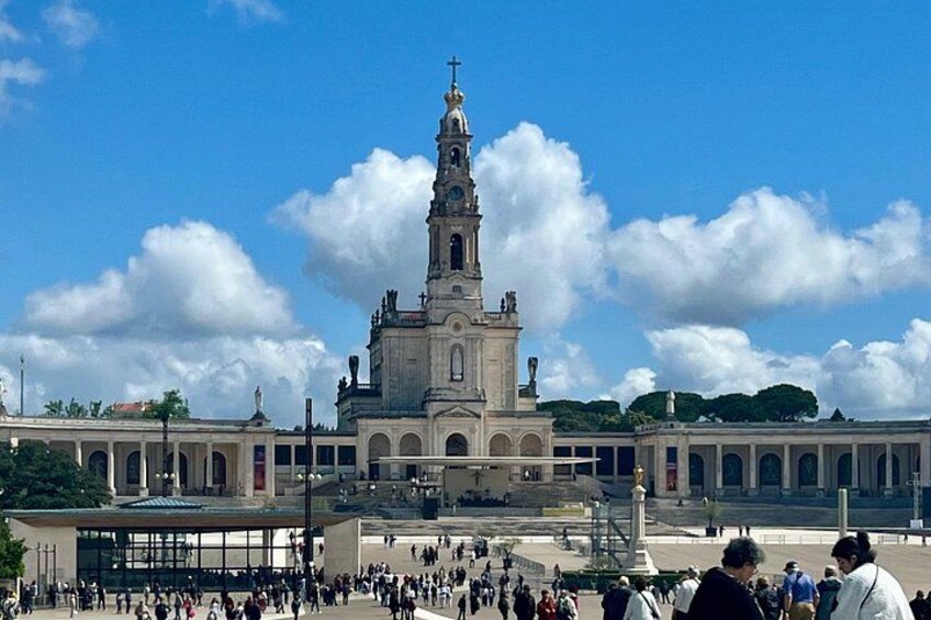 A historic building with a tall tower, a large open plaza, and a crowd of people. 2
