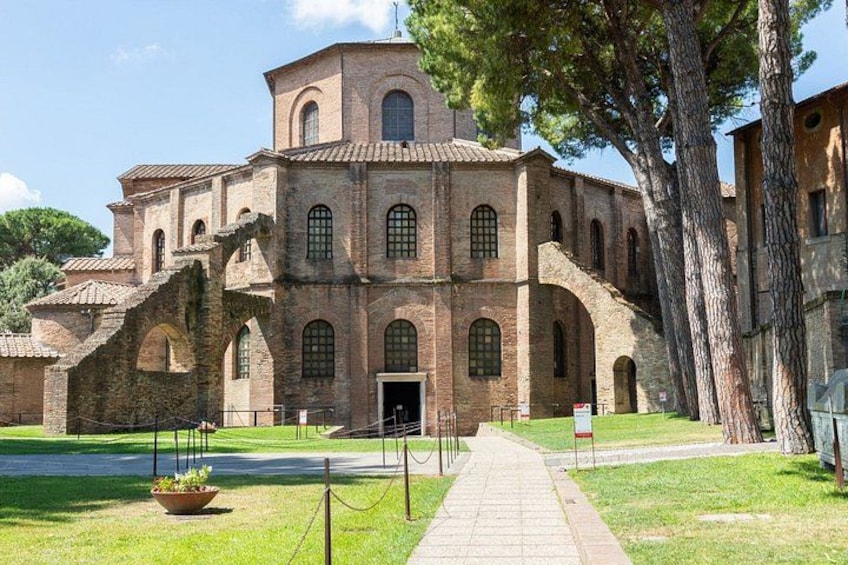 A historic building with arched windows and a central entrance, surrounded by a paved pathway and a grassy area. 2