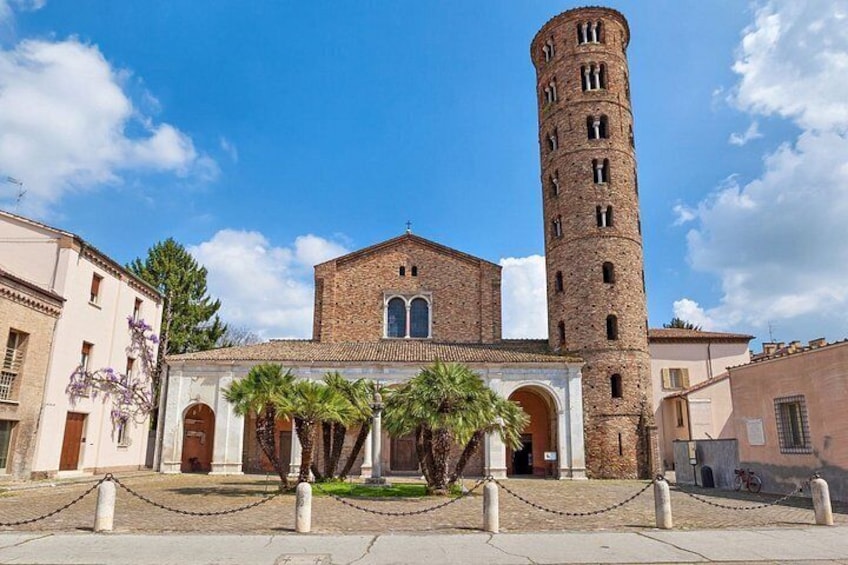 A historic building with a tall tower, arched windows, and a paved courtyard with palm trees. 4