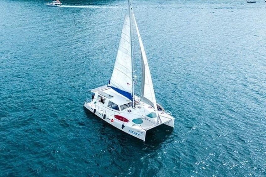 Een witte zeilboot met een blauwe streep op de romp, vaart over blauw water. 1