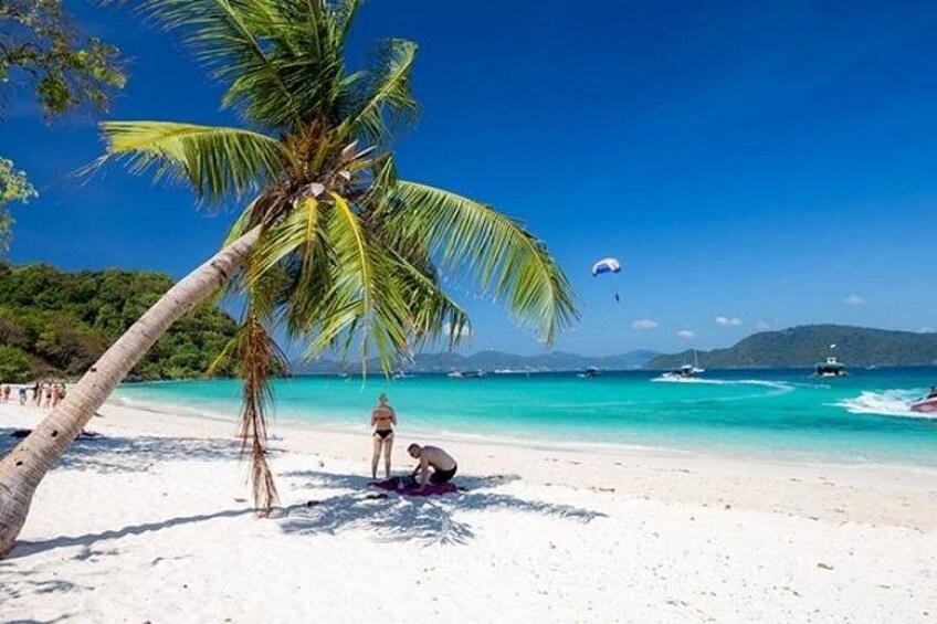 Een strand met een palmboom, helder turquoise water en een persoon die aan het zonnebaden is. 4