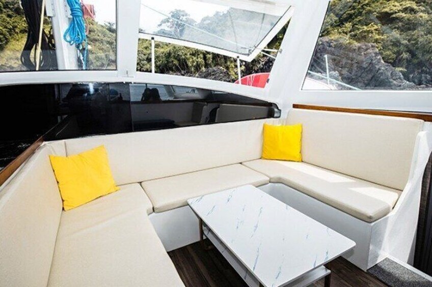 L'intérieur d'un bateau, avec un banc rembourré blanc, une petite table blanche et des coussins jaunes. 3