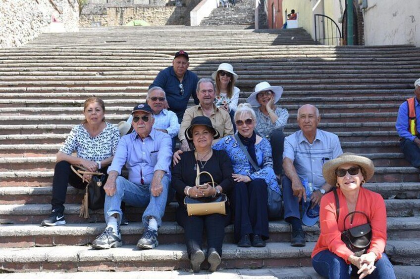 A group of people sitting on stone steps in a historical area. 2