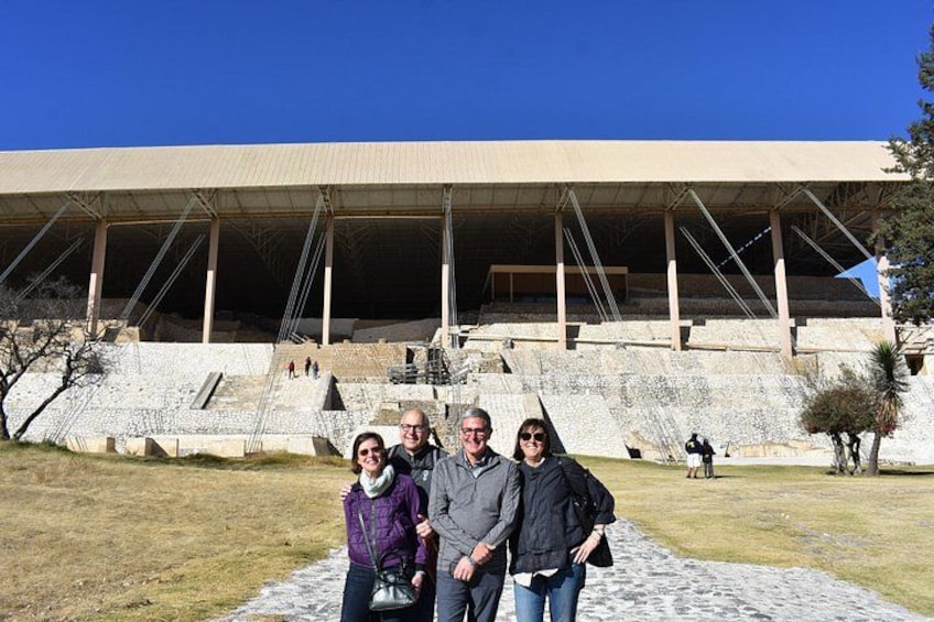 A group of people standing in front of a large, open-air amphitheater with tiered seating. 1