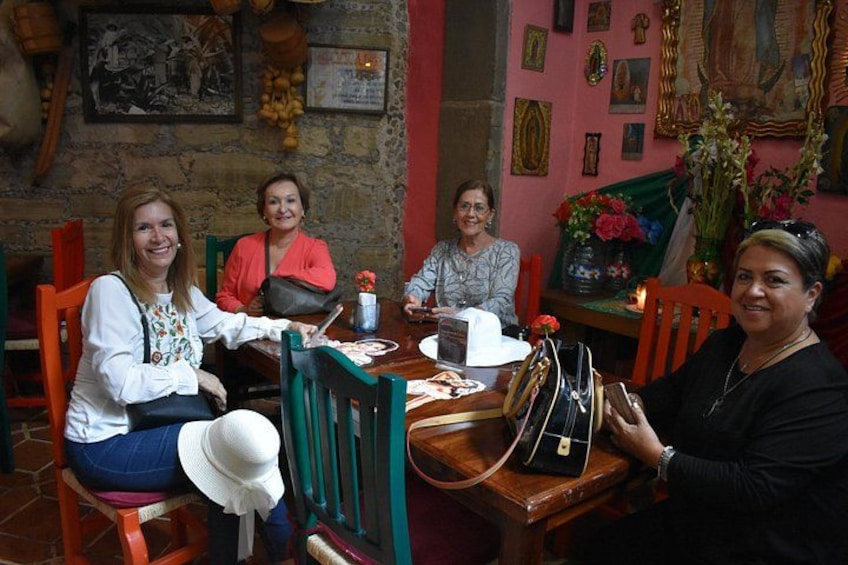 A group of people seated at a wooden table in a room with a brick wall and various framed pictures. 4
