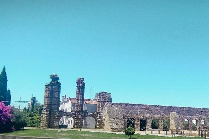 An ancient stone building with columns and arches, surrounded by greenery and a clear sky. 5