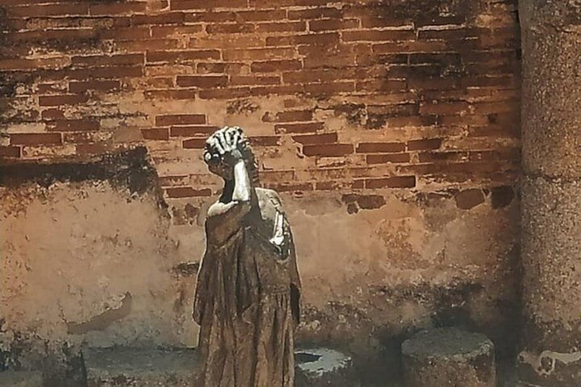 A statue of a person in a long robe standing in front of a brick wall. 2