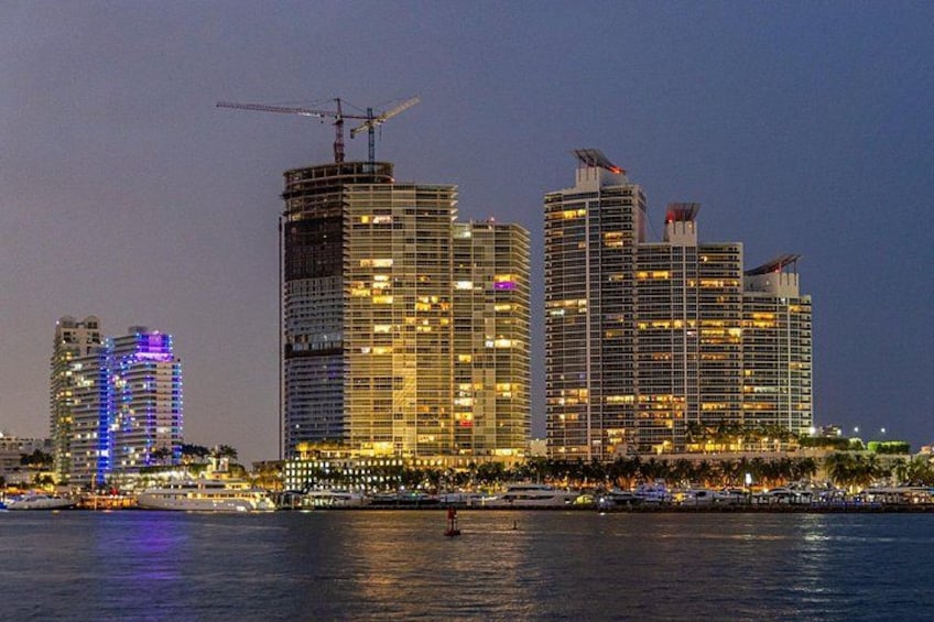 Lo skyline di una città con edifici illuminati, una gru edile e una zona sul lungomare. 4