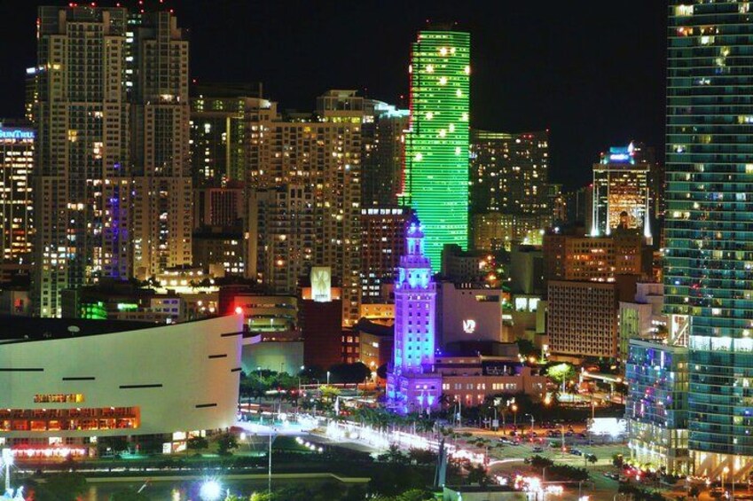 A cityscape at night with illuminated buildings and a prominent green-lit skyscraper. 3