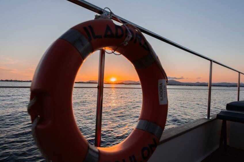 A lifebuoy with 'ILADORA' written on it, a railing, and a sunset over water. 3