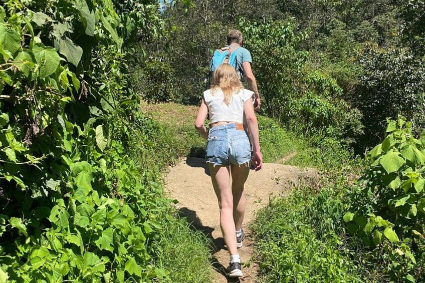 Two people walking on a dirt path surrounded by greenery. 2