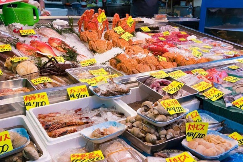 Ein Fischmarkt mit verschiedenen Fischarten, Schalentieren und Meeresfrüchten, präsentiert in Behältern mit Preisangaben. 3