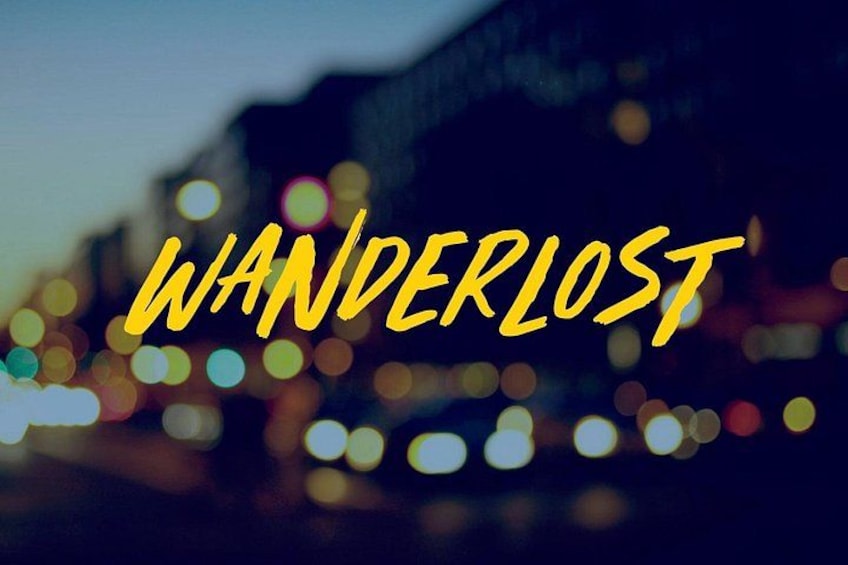 De tekst 'WANDERLOST' in gele letters over een vage stadsgezicht bij nacht. 1