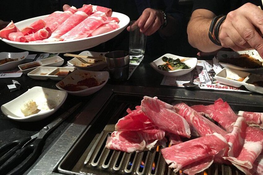 Un gril avec de la viande crue, une assiette de viande tranchée et divers petits plats contenant différents aliments. 2