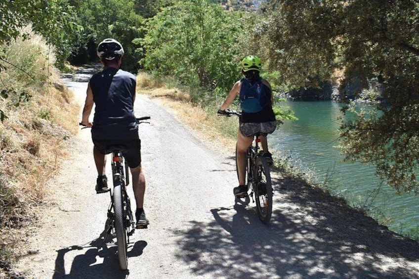 Twee fietsers op een smalle weg langs een rivier, omgeven door groen. 5
