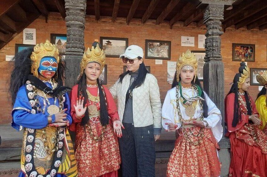 A group of people in traditional costumes with crowns, standing in front of a building with a brick wall and wooden beams. 1