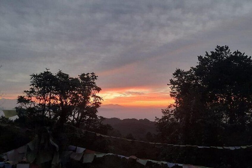 A sunset with trees silhouetted against a colorful sky, a distant mountain range, and a rope barrier in the foreground. 5