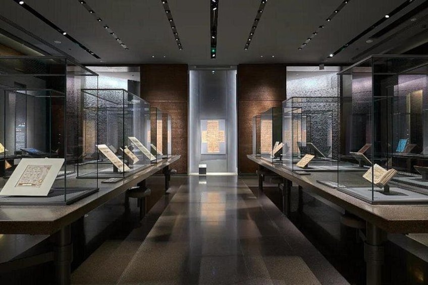 Ein Museuminnenraum mit Glastrennwänden und einem zentralen, beleuchteten Kreuz. 4