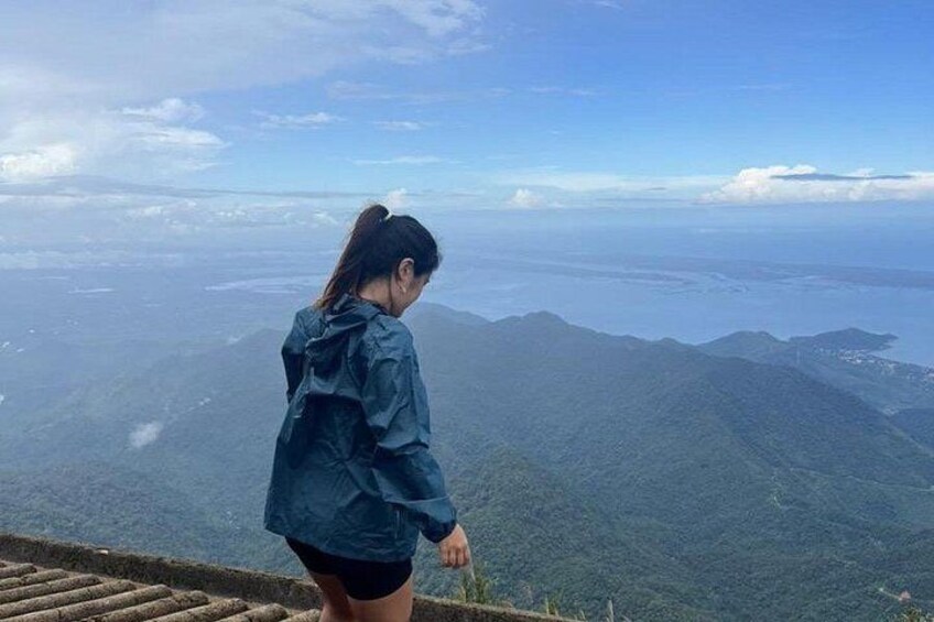Una persona está de pie en la cresta de una montaña, contemplando un extenso paisaje con montañas lejanas y una masa de agua. 2