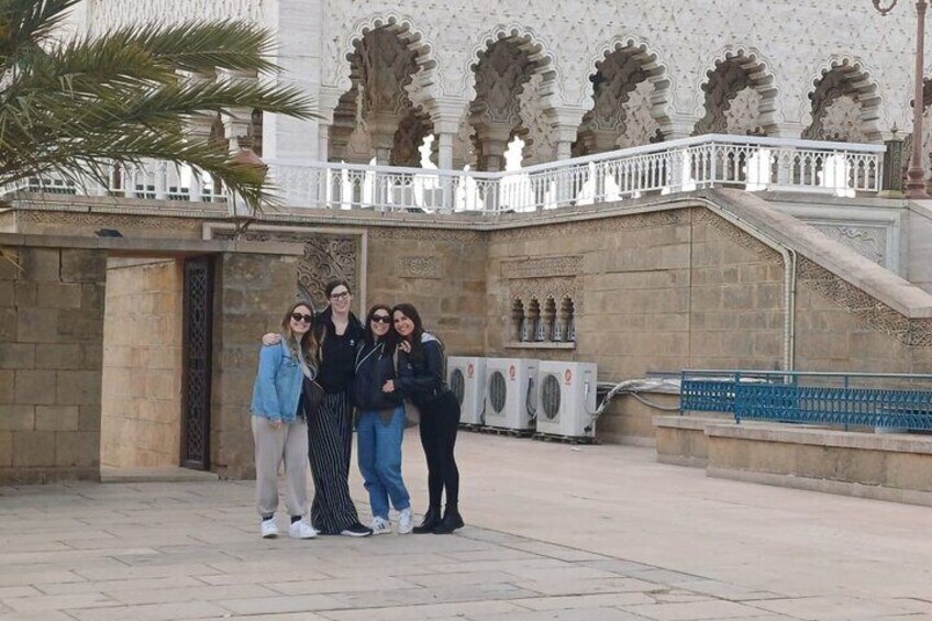 A group of people standing in front of a historic building with ornate arches and a white railing. 2