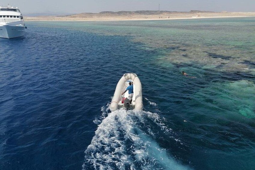 Een boot vaart door helderblauw water, met een zandstrand en een verre kustlijn op de achtergrond. 1