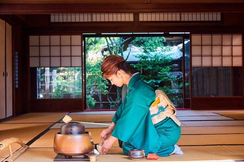 A person in traditional attire performing a tea ceremony in a room with tatami flooring and sliding doors. 2