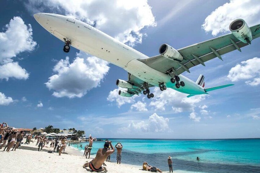 A large white airplane flying low over a beach with people and a boat in the water. 2