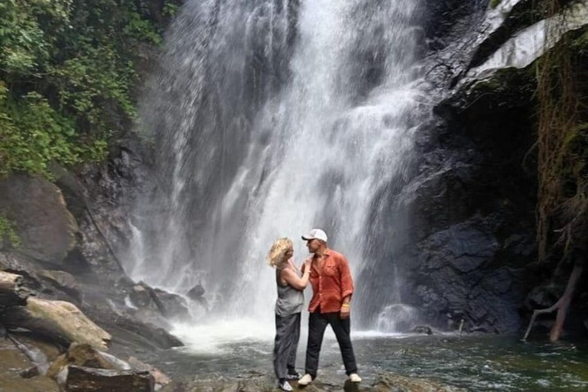 A waterfall with a couple standing in front of it. 1