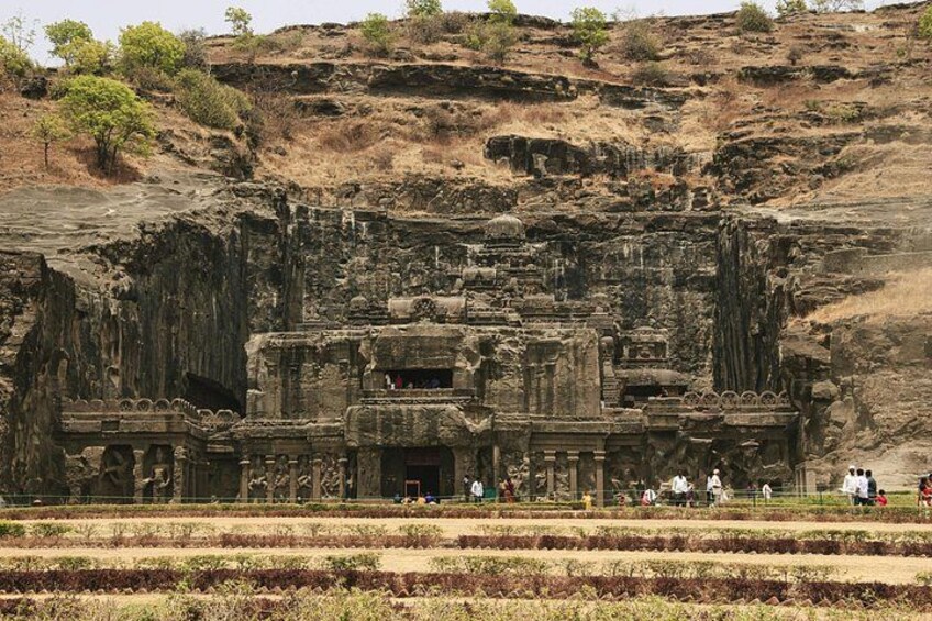 A large ancient rock-cut temple with intricate carvings, surrounded by a dry, hilly landscape. 3