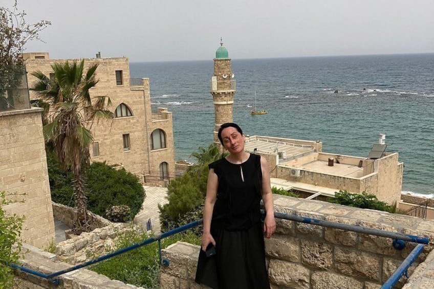 A person standing on a stone staircase overlooking a coastal town with historical buildings and the sea. 4