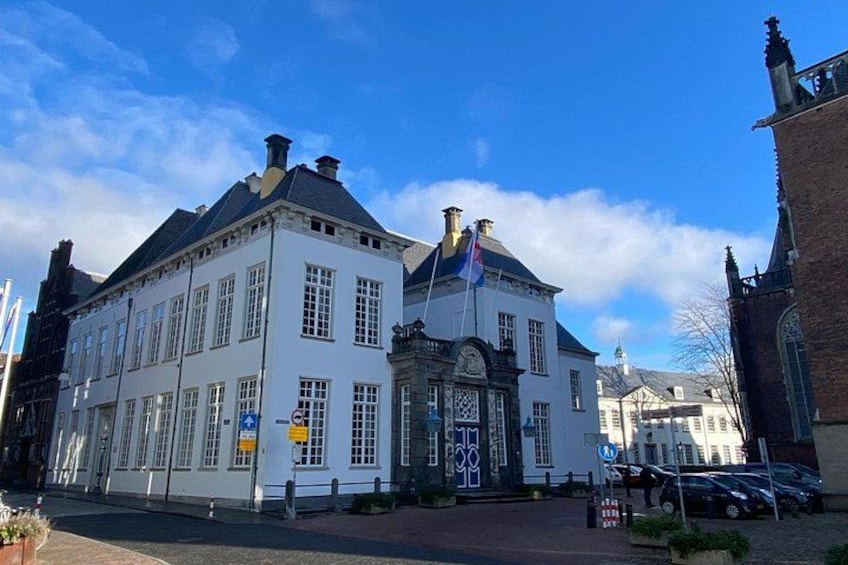 A white building with a black roof, a flag, and a clock tower in the background. 3