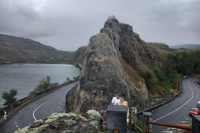 A winding road alongside a large rock formation by a body of water. 3