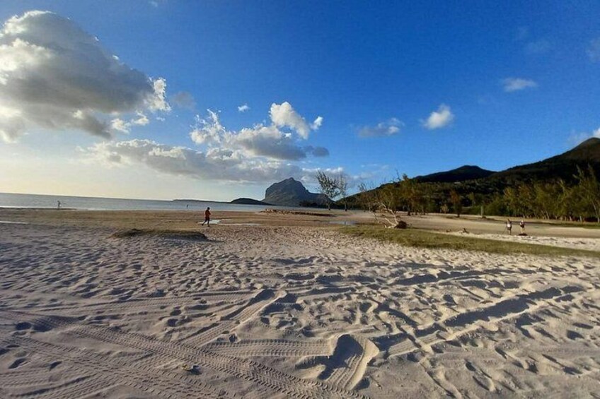 A sandy beach with footprints, a clear sky, and distant hills. 1